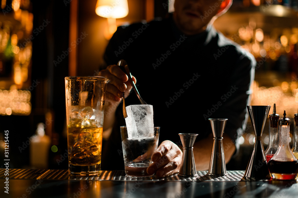 Bartender putting precisely ice cube in cocktail glass - obrazy, fototapety, plakaty 