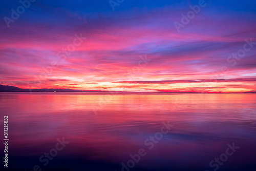 dark violet clouds with orange sun light and pink light in wonderful twilight sky on lake Bodensee in Lindau