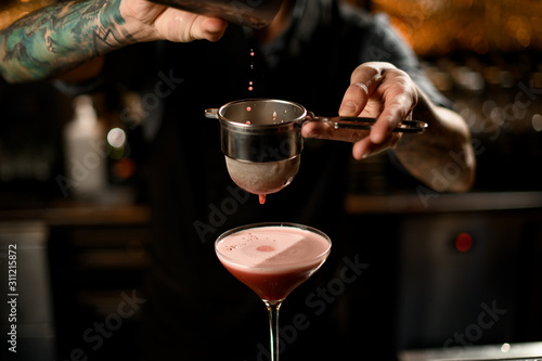 Close-up of bartender pouring drink through sieve