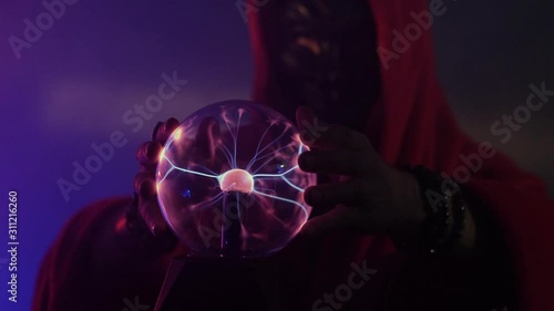 Shaman in hood and mask is touching plasmatron globe and it's react with electrical beam. photo