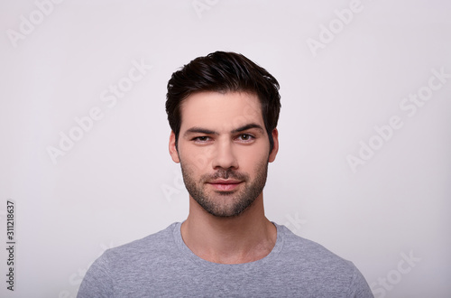 Handsome young man looking at camera while standing against grey background.