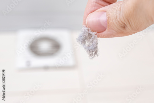 A hand holding dust ib fingers, dirty ventilaion frame on background, dusty home and allergy concept