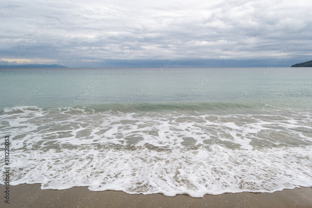 Long calm waves at sea on shore over cloudy sky