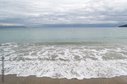 Long calm waves at sea on shore over cloudy sky