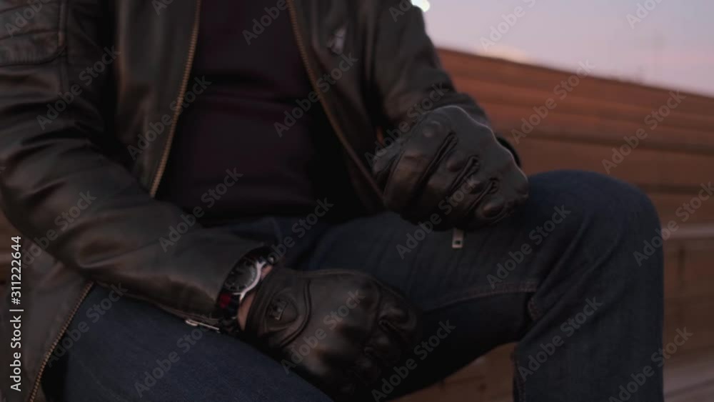 Close-up, a Man in a leather jacket and gloves looking at his watch. Close-up, a Man in a leather jacket and gloves looking at his watch.