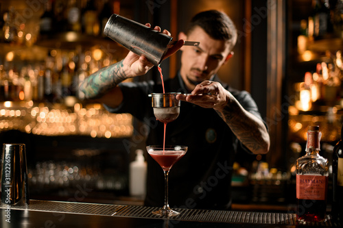 Photography Professional male bartender pouring a alcoholic drink from the steel shaker to t