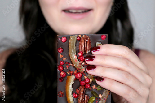 Woman enjoying chocolate, sweet tooth. Girl eating dark chocolate with dried berries, fruit and nuts, tasty dessert, Christmas candy