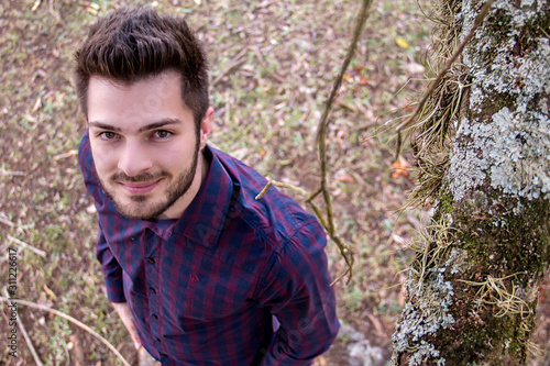 Handsome boy standing touching the trunk of a tree full of textures.