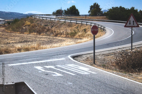 Canvas-taulu Stop sign and markings on the road at a two-way crossroad in a rural countryside