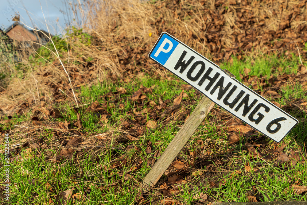 Schiefes Parkplatzschild auf Holzpfeiler für Wohnung 6
