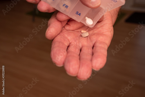 Hand mit Tablettendose leert Inhalt mit Tabletten in Hand einer älteren Person photo