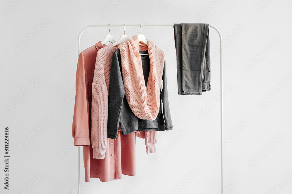 Female clothes in pastel pink and gray color on hanger on white background.  Jumper, shirt, jeans and scarf. Spring/autumn outfit. Minimal concept. - obrazy, fototapety, plakaty 