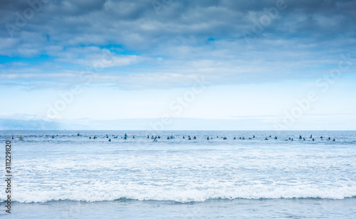 A long line of people on the surfboard waiting for the waves. Day with clouds. An island on the horizon. Concept of freedom and fun