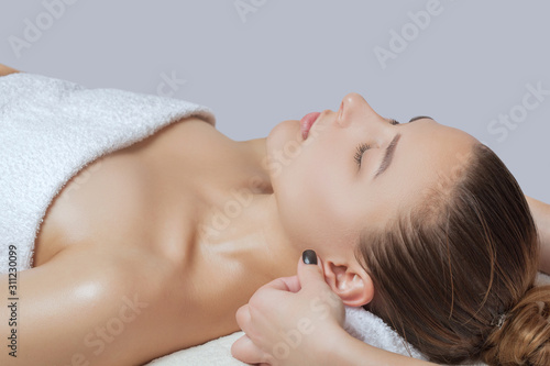 Masseur makes a relaxing massage on the ears  face  neck  shoulders and collarbones of a young beautiful woman in a spa. Cosmetology and massage concept.