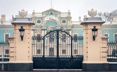 gate iron entrance of an old blue baroque building with lawn, decorative tree and boxwood bushes, Mariinsky Palace in Kiev, Ukraine.