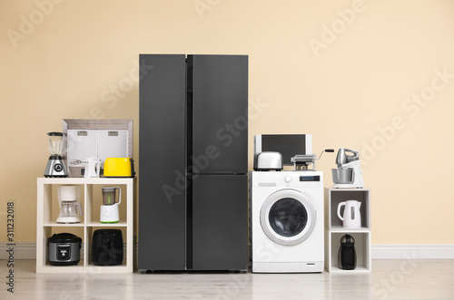 Fotografi Modern refrigerator and other household appliances near beige wall indoors