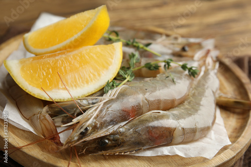 Fresh raw shrimps with lemon slices on table, closeup