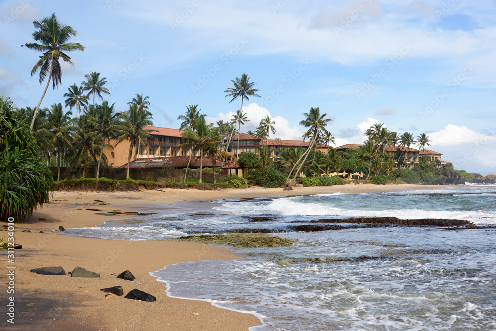 Waves crashing onto the beach at Galle, overlooked by luxury property