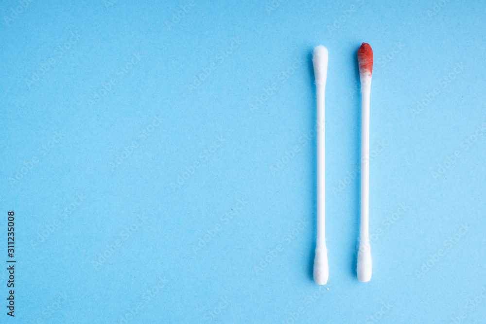 Blood on the hygiene cotton stick. Menstruation. Skincare mockup for design. Stack of disposable cotton stick on a blue background. Cosmetology concept. Bloody wound. Injury.