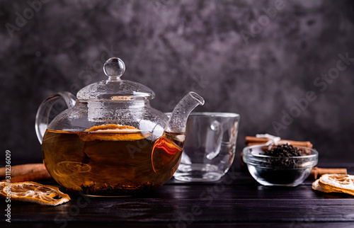glass teapot of black tea with lemon on dark background