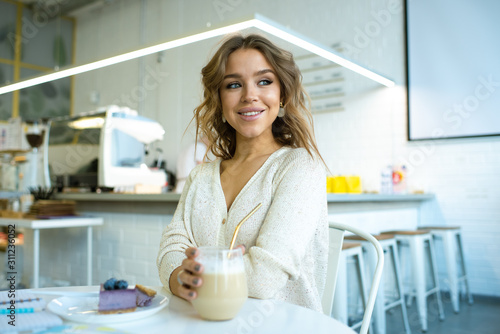 Pretty young smiling woman having glass of cappuccino with cheesecake
