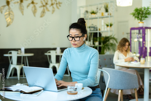 Pretty young casual woman with wireless earphones typing in front of laptop