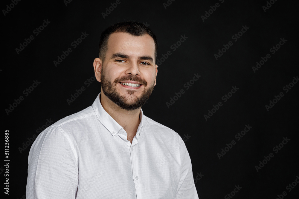 Close-up portrait of smiling handsome bearded man looking at camera on black background