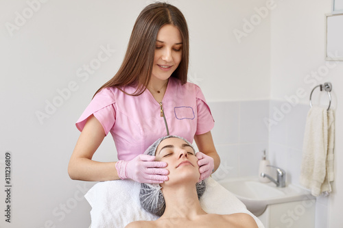 Canvas Print Image of careful positive cosmetologist making anti wrinkle facial massage, wearing pink lab coat and gloves