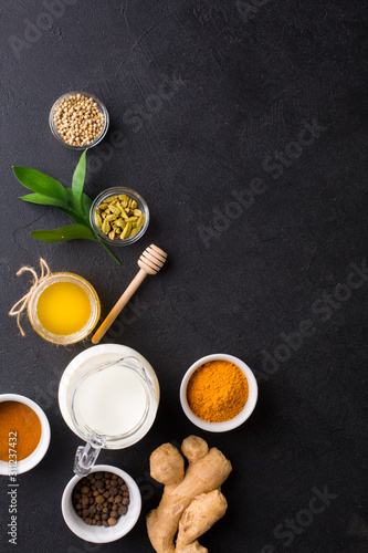 Ingredients for Golden Latte on black background. Ginger root, milk, honey, cinnamon, turmeric, cardamom, allspice peas