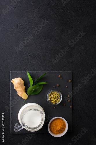 Ingredients for Golden Latte on black background. Ginger root, milk, turmeric, cardamom, allspice peas