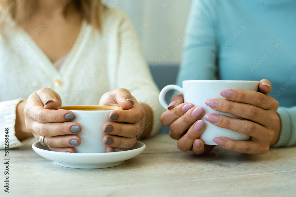 Hands of two young friendly females in casualwear holding cups with coffee Hands of two young friendly females in casualwear holding cups with coffee