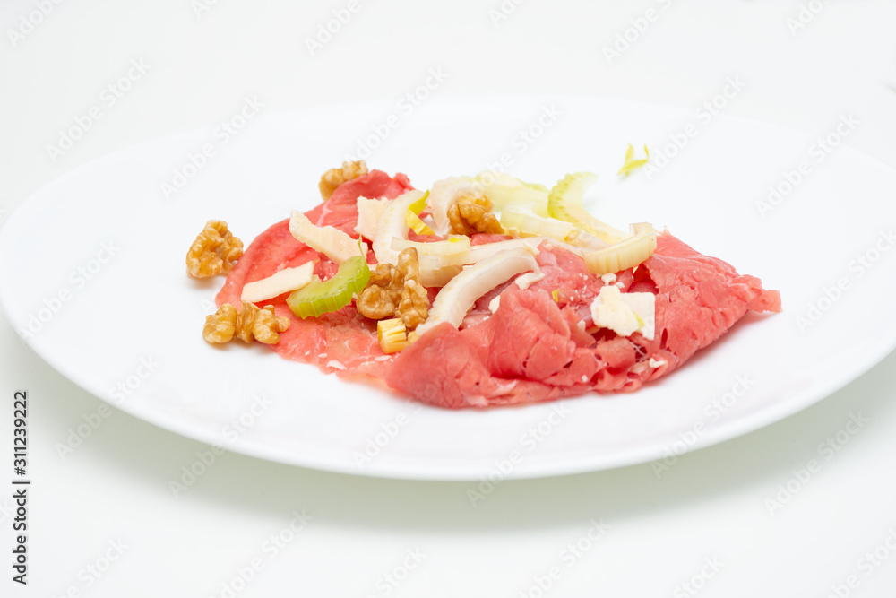 albese meat with savoy cabbage, walnuts, celery and parmesan cheese in the foreground on plate and white background albese meat with savoy cabbage, walnuts, celery and parmesan cheese in the foreground on plate and white background