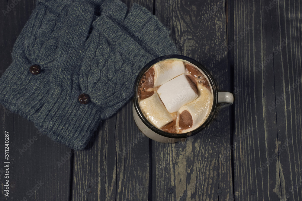 Tasty marshmallows in an old white iron retro mug with aromatic coffee or cocoa, with mittens and gloves on a black wooden background Tasty marshmallows in an old white iron retro mug with aromatic coffee or cocoa, with mittens and gloves on a black wooden background