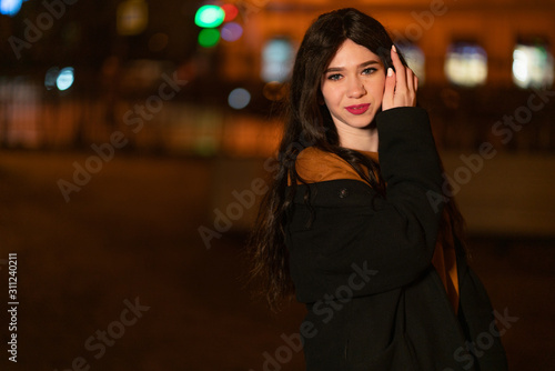 beautiful portrait of a girl in an autumn jacket. girl in a night city surrounded by houses and the warm light of lanterns © Alex
