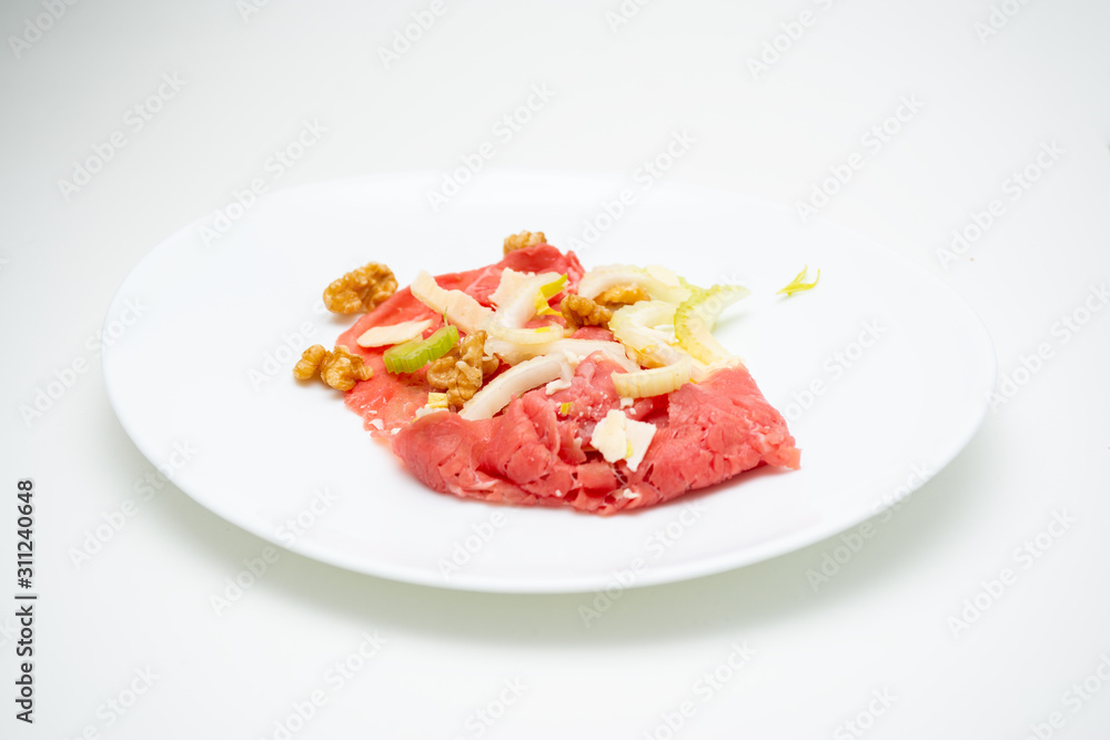 albese meat with savoy cabbage, walnuts, celery and parmesan cheese in the foreground on plate and white background albese meat with savoy cabbage, walnuts, celery and parmesan cheese in the foreground on plate and white background