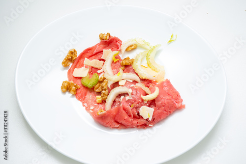 albese meat with savoy cabbage, walnuts, celery and parmesan cheese in the foreground on plate and white background