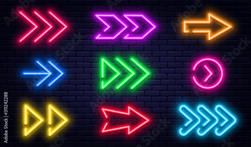 Set of glowing neon arrows. Glowing neon arrow pointers on brick wall background. Retro signboard with bright neon tubes in red, yellow, purple and blue colors photo