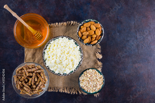 Healthy diet breakfast on burlap. Ingredients for a healthy breakfast - oatmeal, granola, honey, almonds, cottage cheese. Homemade granola on a dark background. Rustic style