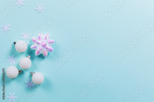 Blue background with white Christmas decorations and holographic bow. Holiday concept. Flat lay  copy space