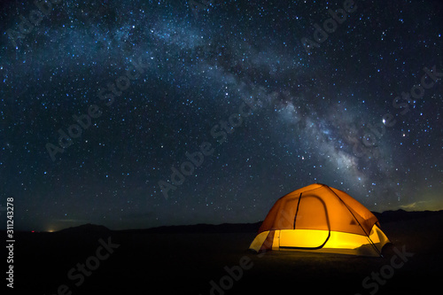 Lit tent on the playa under a bright Milky Way arch of stars photo