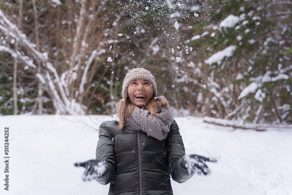 Happy woman catching snowflakes on the walk in snowy winter forest. Spending vacations outdoor, seasonal activities concept
