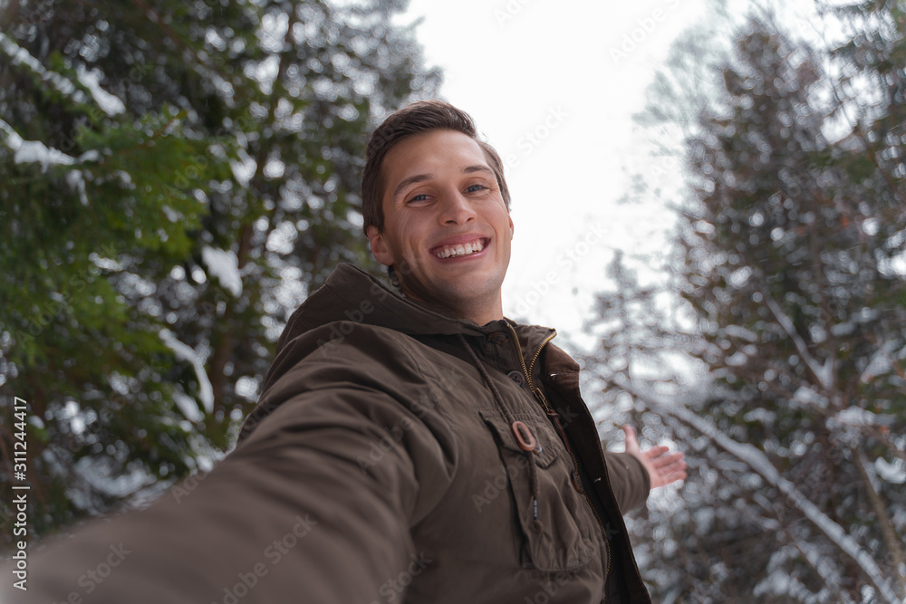 young man taking a self portrait picture and smiling in the nature during winter season young man taking a self portrait picture and smiling in the nature during winter season