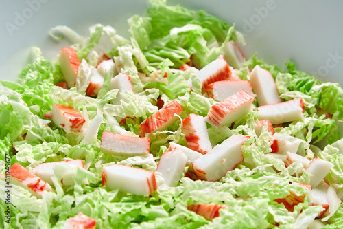 Pieces of crab sticks and fresh chinese cabbage leaves chopped in white ceramic bowl on black stone background. Green vegetable and imitation crab meat, sea food. Cooking salad