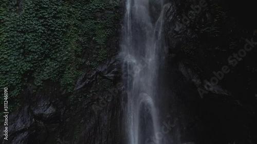 Aerial drone shot Flying into almost inside to a hidden green Yeh Mempeh waterfall, Bali, Indonesia in a rainforest on a bright day. No color correction, no edit photo