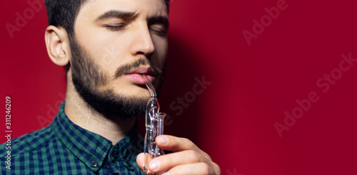 Close-up studio portrait of young man doing respiration treatment with classic inhalator and essential oil. Isolated on red background.