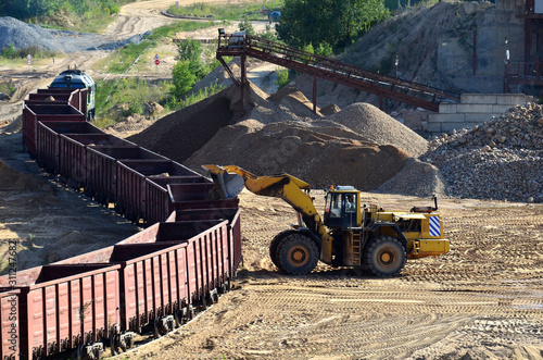 Large heavy front-end loader loading sand it to the freight train. Heavy mining work in a quarry