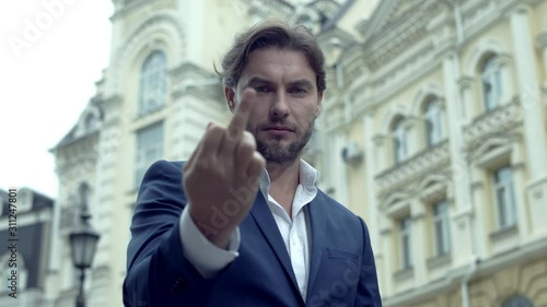Portrait of an attractive man dressed in a blue suit on a city background. Fuck you sign