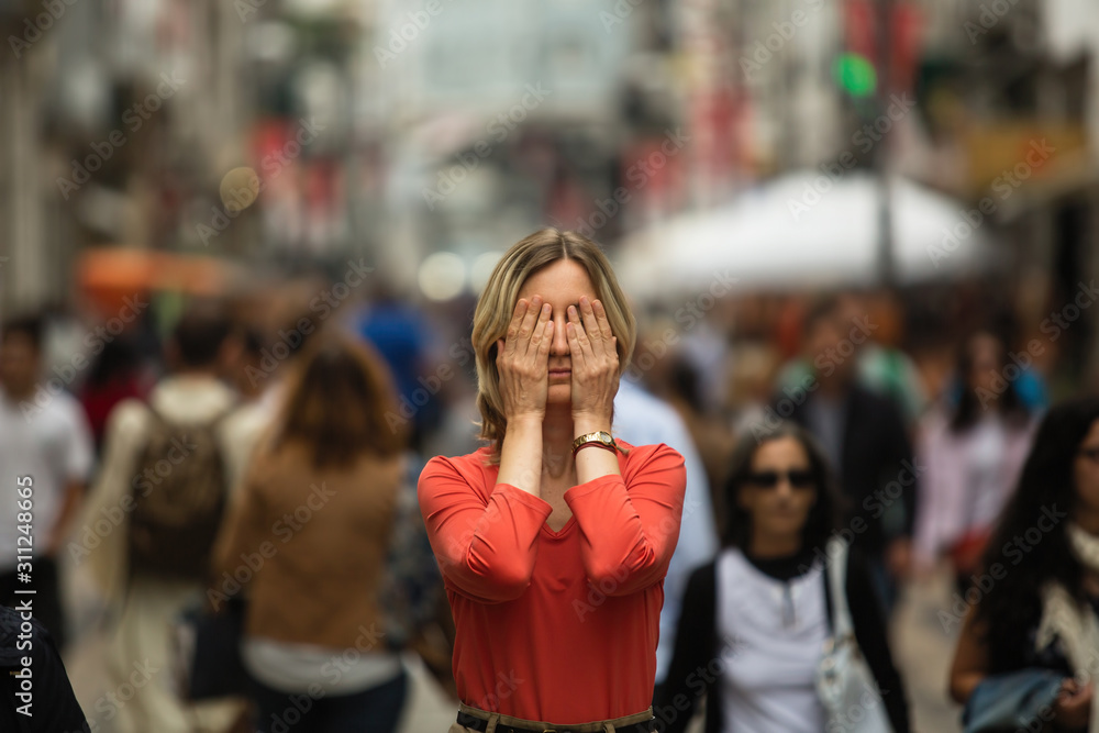 Young woman covers his eyes at standing in the middle of a crowded street.