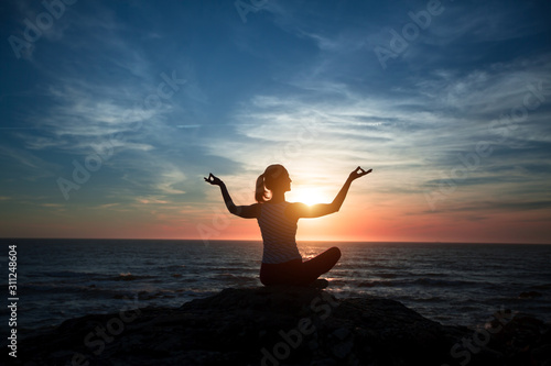 Silhouette of yoga woman sitting on the ocean beach during wonderful sunset.