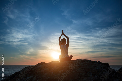 Yoga woman silhouette sitting in Lotus position on the ocean beach during magnificent sunset.